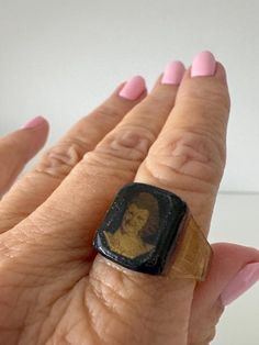 a woman's hand wearing a ring with a gold and black portrait on it