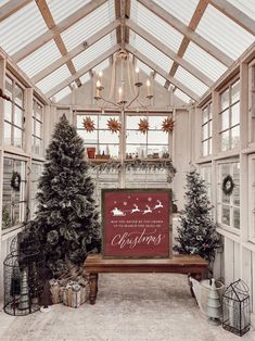 a christmas display in a greenhouse with trees and presents on the bench, lights hanging from the ceiling