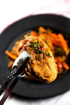 a black plate topped with meat and veggies next to a fork on top of a table