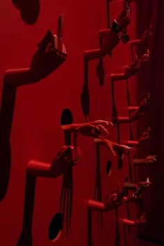 there are many forks and spoons hanging on the wall with red walls behind them