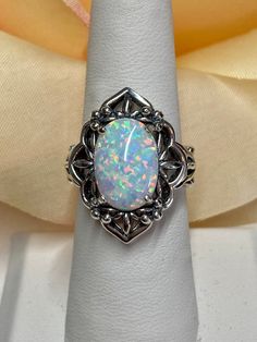 Simulated Opal Gemstone Ring  Oval Mesh Design#98 Custom Made This is a lovely Gothic inspired sterling silver filigree ring.  The stunning rainbow white simulated opal is 14mmx 10mm in length and width.  The setting is 24mm North/South on the finger.  The inside of the band is marked 925 for sterling silver. The filigree has a subtle floral design that accents the dazzling center stone.  This unusual gothic ring is  an amazing mixture of sophisticated style combined with an expressive elegance. Heirloom Style Oval Opal Ring, Formal Silver Cabochon Opal Ring, Formal Silver Opal Cabochon Ring, Antique Oval Opal Ring In Sterling Silver, Formal Oval Opal Ring In Sterling Silver, Classic Silver Opal Ring Oval Cabochon, Vintage Silver Opal Ring With Oval Shape, Vintage Silver Oval Opal Ring, Ornate Silver Jewelry With Accent Stones