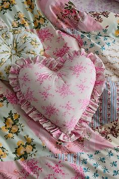 a heart shaped pillow sitting on top of a bed covered in pink and yellow flowers