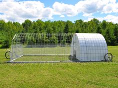 a large metal structure sitting on top of a lush green field next to a forest