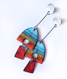 two colorful earrings hanging from hooks on a white surface