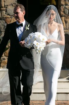 the bride and groom are walking down the aisle with white flowers in their bouquets