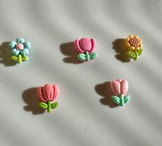 four different colored flower shaped buttons on a white tablecloth with shadows from the top