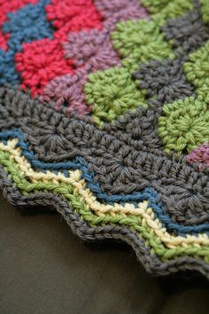 a crocheted blanket is laying on a black surface with green, red and blue colors