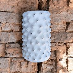 a white vase sitting on top of a stone wall next to a brick wall with holes in it