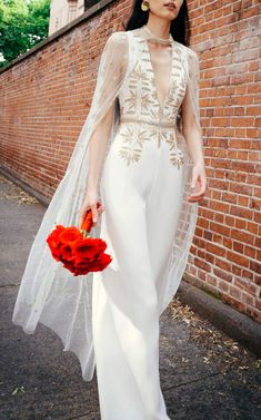 a woman is walking down the street wearing a white dress and holding a red bouquet