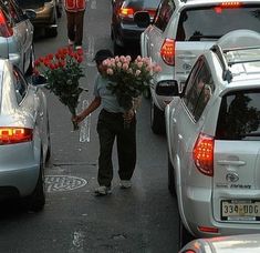 a man is walking down the street with flowers in his hand and cars behind him