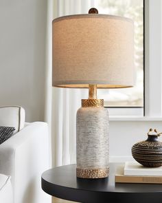 a table with a lamp on top of it next to a book and a vase