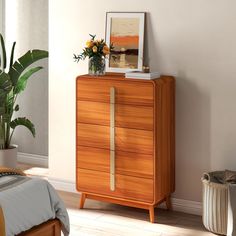 a bedroom with a wooden dresser next to a bed and potted plant on top of it