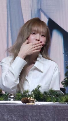 a woman covering her mouth while sitting in front of a christmas display with pine cones and greenery