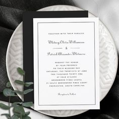 an elegant black and white wedding card on top of a plate with greenery next to it