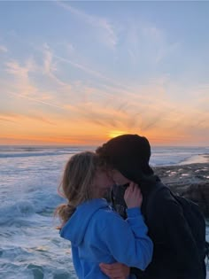 a man and woman are kissing on the beach at sunset with waves in the background