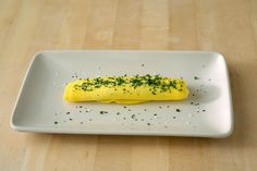 a white plate topped with an omelet covered in cheese and chives on top of a wooden table