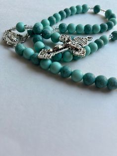 "This beautiful rosary features large solid and marble turquoise beads interchanging throughout the piece. The beads are 10MM and run through the hand seamlessly. The total length of the rosary is 17 inches. Clear spacer beads have been added to further separate the decades from the Our Father beads. The centerpiece is a large medal that has the inscription \"Immaculate Heart of Mary Pray for Us\" on the back. A large Pardon Crucifix that reads \"Father Forgive Them\" is paired. The rosary is st Turquoise Rosary Bracelet With Round Beads, Turquoise Spiritual Rosary Bracelet With Round Beads, Spiritual Turquoise Rosary Bracelet With Round Beads, Spiritual Turquoise Necklace With 8mm Beads, Turquoise Rosary With Round Beads, Spiritual Turquoise Rosary With Round Beads, Turquoise Rosary With Round Beads As Gift, Father Forgive Them, Pray For Us