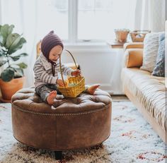 a small child sitting on top of a brown ottoman