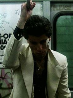 a man in a white suit holds his cell phone up to his ear while riding the subway