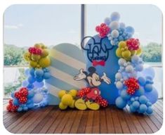 a mickey mouse balloon arch with balloons on the floor in front of a large window