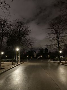 an empty street at night with lights on and trees in the foreground that are bare