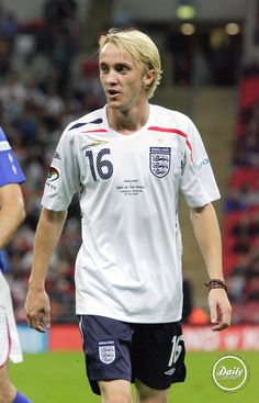 a soccer player with blonde hair and blue shorts is on the field in front of an audience