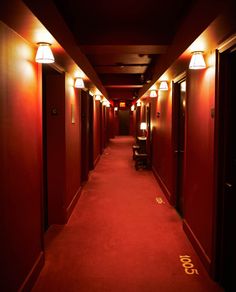 a long hallway with red walls and lights on either side of the corridor is lit by two lamps