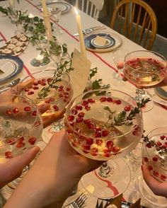 people holding up wine glasses filled with food and garnished with greenery on the table