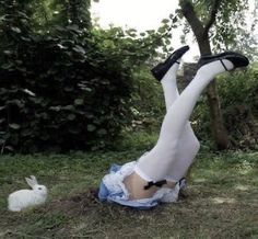 a woman laying on the ground with her legs up next to a white rabbit in a field