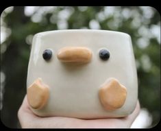 a close up of a person holding a ceramic object with two eyes and nose shapes