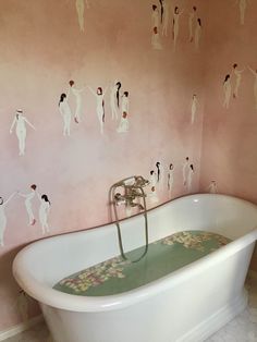 a bath tub sitting in a bathroom next to a wall with people painted on it