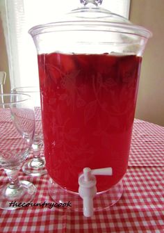 a pitcher filled with liquid sitting on top of a red checkered table cloth next to wine glasses