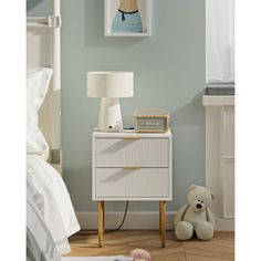 a white night stand with two drawers and a teddy bear on the floor next to it