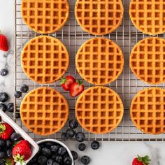 six waffles on a cooling rack with strawberries and blueberries next to them