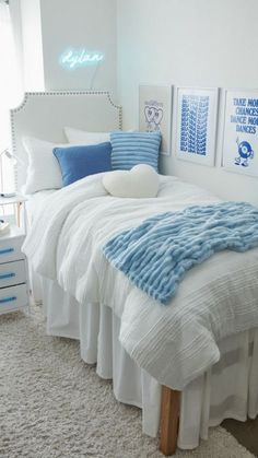 a white bed with blue and white pillows in a bedroom next to a wall mounted art