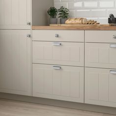 a kitchen with white cabinetry and wood flooring is pictured in this image, there are bread on the counter