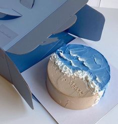 a blue and white cake in a box on top of a table next to a knife