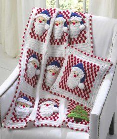 a crocheted christmas blanket with santas and snowmen on it, sitting next to a white chair