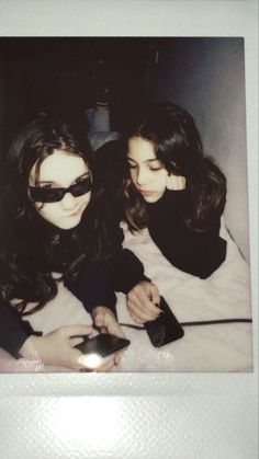 two young women laying on top of a bed next to each other holding remote controls