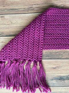 a purple knitted scarf with tassels laying on top of a wooden floor