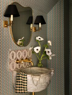 a sink and mirror in a room with wallpaper on the walls, flowers are placed next to it