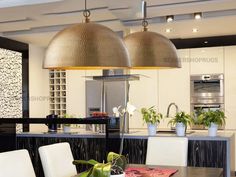 two lamps hanging over a kitchen table with white chairs and potted plants on it