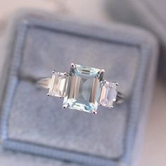 an emerald cut ring with three baguettes sits in a velvet box on the table