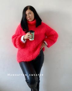 a woman wearing black leather pants and a red sweater holding a cup in her hand