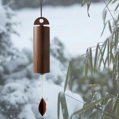 a wind chime hanging from a tree in front of snow covered trees and bushes