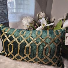 a green and gold pillow sitting on top of a white furnishing next to a vase with flowers