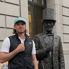 a man standing next to a statue of a man with a top hat and vest