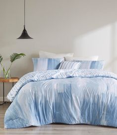 a bed with blue comforter and pillows in a white room next to a table