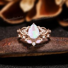 an opal and diamond ring sits on top of a piece of wood next to some flowers