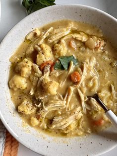 a bowl of chicken noodle soup on a white plate with a spoon in it